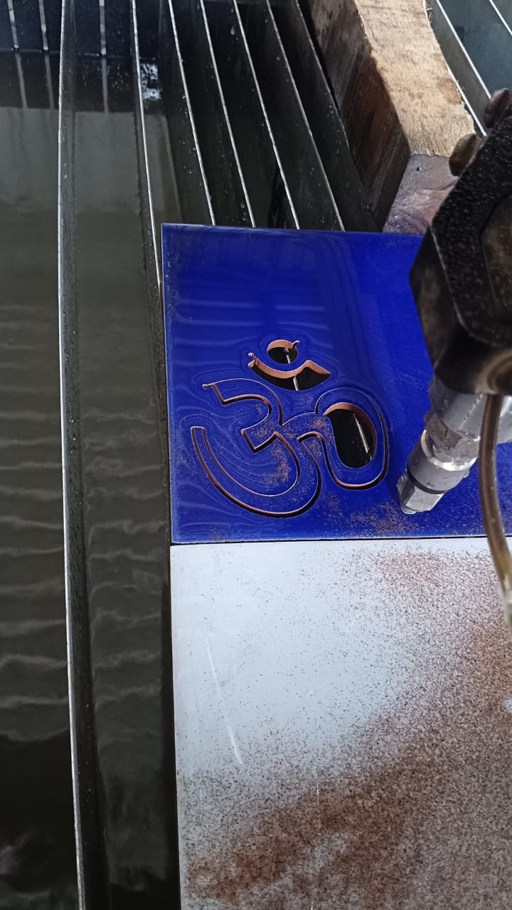 Om symbol being water jet cut from blue sheet metal